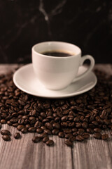 A cup of coffee and coffee beans on a dark background. Roasted coffee beans.