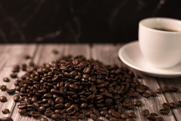 A cup of coffee and coffee beans on a dark background. Roasted coffee beans.