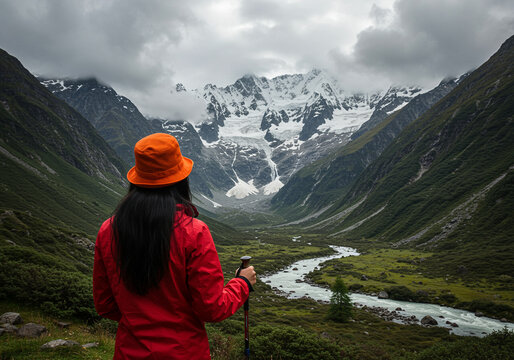 Person in red jacket hiking in mountain valley with snowy peaks under cloudy sky enjoying mountain view and hiking adventure