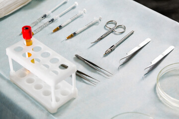 Hair transplant surgery tools: tweezers, needles, and a blood vial on a sterile table