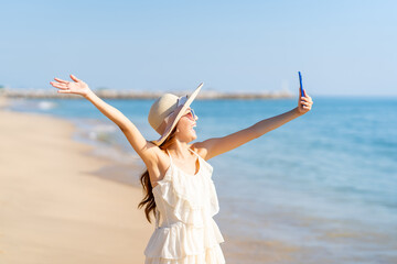 Happy woman using mobile phone taking selfie or vlogging during travel nature the sea on summer beach holiday vacation. Attractive girl enjoy and fun outdoor lifestyle using smartphone at the beach.