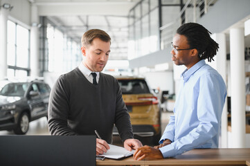 Dealer with male customer signing documents at auto salon. Bearded man in buying new vehicle at car center