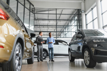 Car Sales Manager Showing Auto To Buyer Standing In Luxury Automobile Dealership Store