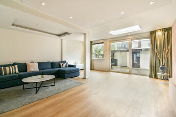 A spacious and stylish living room featuring a plush sofa, wooden flooring, and large windows allowing natural light to illuminate the area.