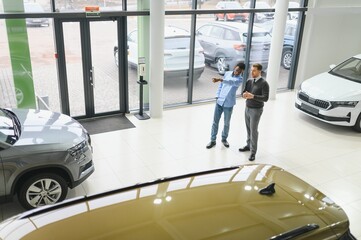 A consultant at a car dealership helps a customer choose a new car.