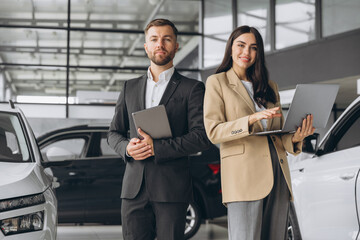 Super sales team in dealership, two consultants or managers in elegant suits with laptop and tablet...