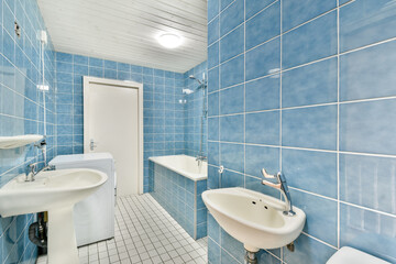 A clean and contemporary bathroom featuring blue tiled walls, white fixtures, and ample lighting,...