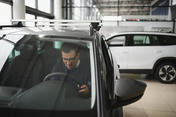 Young man is choosing a new vehicle in car dealership