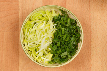 A small bowl contains chopped leeks and scallions, neatly separated into two distinct sections