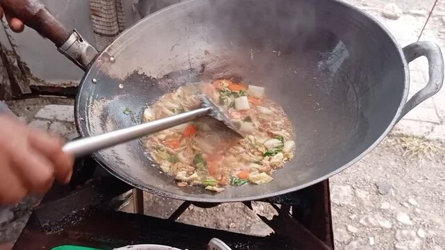 A streetside Chinese food vendor is cooking capcay ordered by his customer, Chinese food stall, Indonesian food.