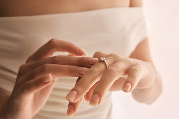 Close-up of female hands gently placing engagement ring with prominent stone onto ring finger...
