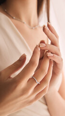 Close-up of young woman tender hands displaying a delicate curved ring and slightly visible necklace against a softly focused background. Concept of jewelry, luxury, accessories, beauty
