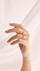 Cropped image of tender female hand with manicured nails wearing two delicate rings against a...