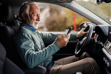 Senior driver driving a car and typing mobile phone.