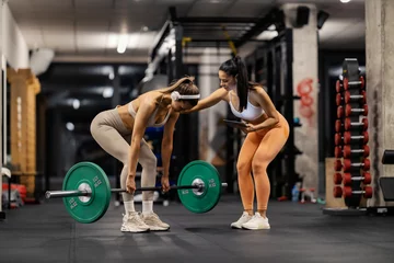 Fotobehang Persoonlijk Young fit strong sportswoman lifting barbell at gym while her personal trainer is motivating her.  © Dusan Petkovic
