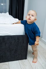 Cute blond toddler boy in blue t-shirt running in spacious hotel room. Toddler boy in comfortable hotel room resting after travel. Child at home sitting on floor