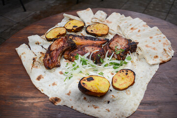 Grilled meat. Pork barbecue. Fried meat with onions, potatoes wrapped in pita bread. Lamb steak on pita bread with grilled potatoes on wooden table. Restaurant food. Fast food