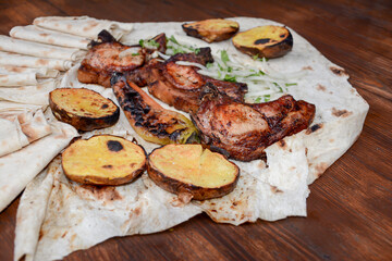 Grilled meat. Pork barbecue. Fried meat with onions, potatoes wrapped in pita bread. Lamb steak on pita bread with grilled potatoes on wooden table. Restaurant food. Fast food