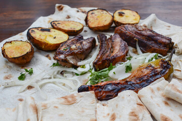 Grilled lamb ribs with grilled potatoes and herbs on pita bread. Pork barbecue. Potato bbq. Fried lamb on a table. Fast food. Restaurant food