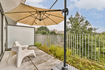 A stylish balcony featuring a canopy umbrella and a minimalist chair, accented by greenery and a serene urban view.
