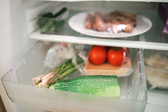 Plate of leftover sausages on shelf of fridge surrounded by vegetables