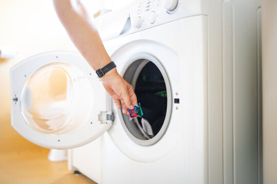 Person placing laundry detergent capsule in front loader washing machine