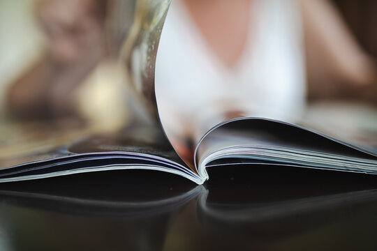 Open magazine on coffee table with out of focus woman in background