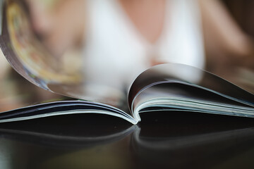 Open magazine on coffee table with out of focus woman in background