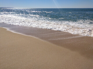 A serene beach at midday with gentle waves lapping the shore and clear blue skies inviting...