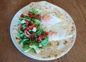 Delicious breakfast with fried eggs, fresh salad, and flatbread served on a wooden plate