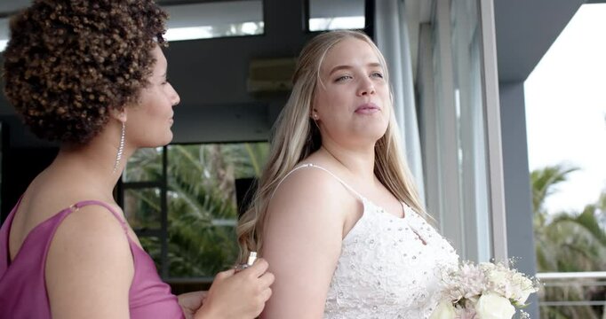 Happy bride and bridesmaid smiling, talking and preparing before a wedding in bedroom