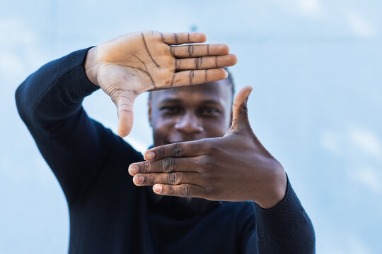 Young African American guy showing camera shape gesture with hands looking through at camera, picking best position for making picture