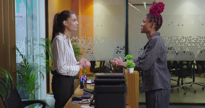 Happy young adult gen z woman lady staff agent standing desk table do help check email data give key card client visit in office Asian female girl talk share enquiry to visitor at job place day time