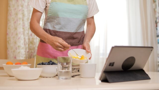 Woman adding ingredients while cooking using digital tablet recipe