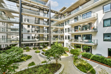 A contemporary apartment complex featuring a vibrant courtyard filled with plants and trees, creating a serene living space amidst urban architecture.