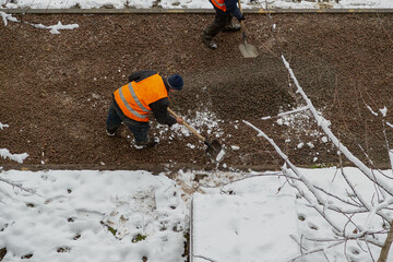 Workers are leveling a layer of gravel with shovels on a gravel road, construction work in winter, construction services are carrying out road improvement using manual labor.