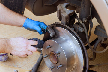 Technician works on vehicle's brake system, adjusting components with care precision in well lit workshop.