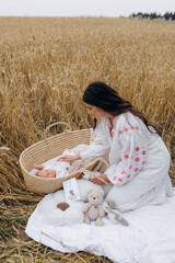 Mother playing with 1 month old son in crib in wheat field on picnic. Newborn boy