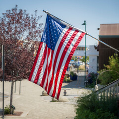 Naklejka premium The American flag, the Stars and Stripes, flying outside a building in a typical american main street, on a sunny day