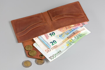 Unfolded classic brown leather wallet with banknotes inside and coins