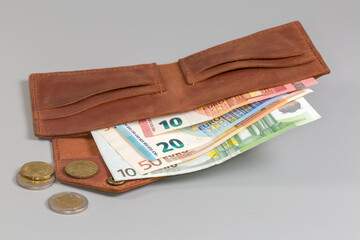 Unfolded classic brown leather wallet with banknotes inside and coins