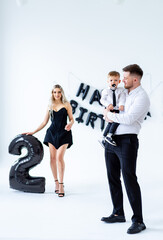 Fototapeta premium 2nd birthday bash for boy. A woman in black with a little boy in formal attire celebrates his second birthday with balloons and decorations.