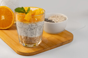 Chia pudding with fresh orange and oatmeal in a glass on a light background with space for text. Healthy eating. Diet.
