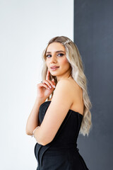 Fototapeta premium Elegant young woman in modern clothes. A young woman wearing a stylish black dress poses gracefully with a charming smile in a minimalist studio setting.