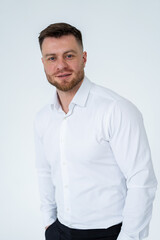 Man in white shirt poses confidently. A man stands confidently in a white shirt, smiling warmly at the camera in a neutral background.