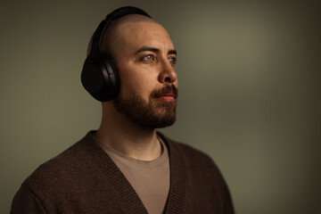 Obraz premium Portrait of a focused man with a beard wearing black over-ear headphones, listening intently against a dark, moody background. Ideal for music, podcasting, and audio technology concepts.