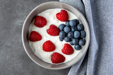 Gray bowl and natural yogurt with berries on the stone black background.