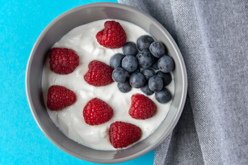 Gray bowl and natural yogurt with berries on the blue background.