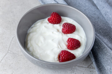 Gray bowl and natural yogurt with berries on the stone marble table.