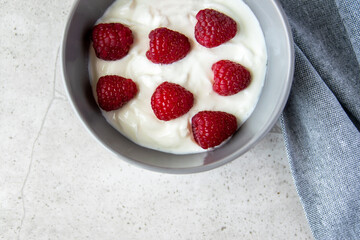 Gray bowl and natural yogurt with berries on the stone marble table.